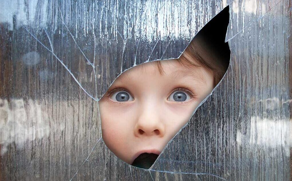 Child looking through sharp edged hole in broken glass
