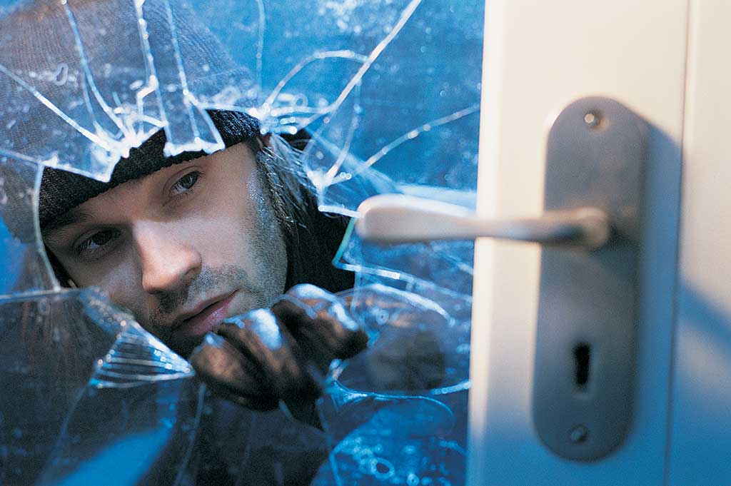 Intruder reaching in through broken glass to open a door