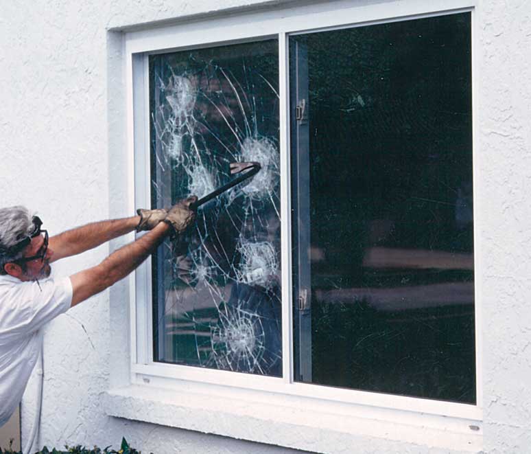 Window with security film being broken by a man with a crow bar