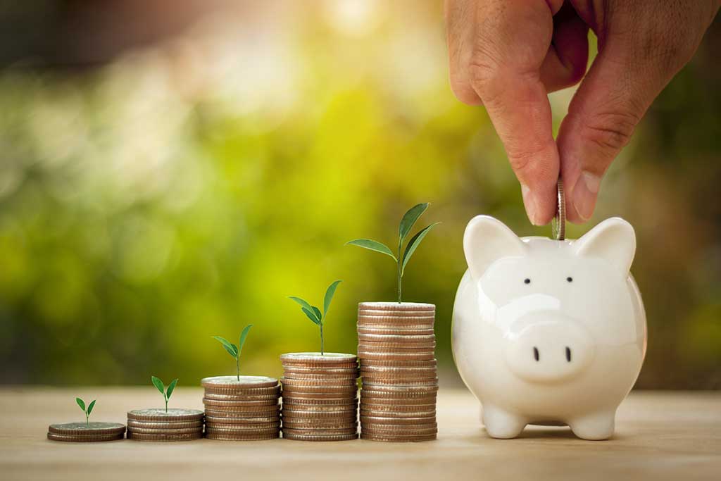 Man putting coins into piggy band next to stacks of quarters with plants growing out of the tops