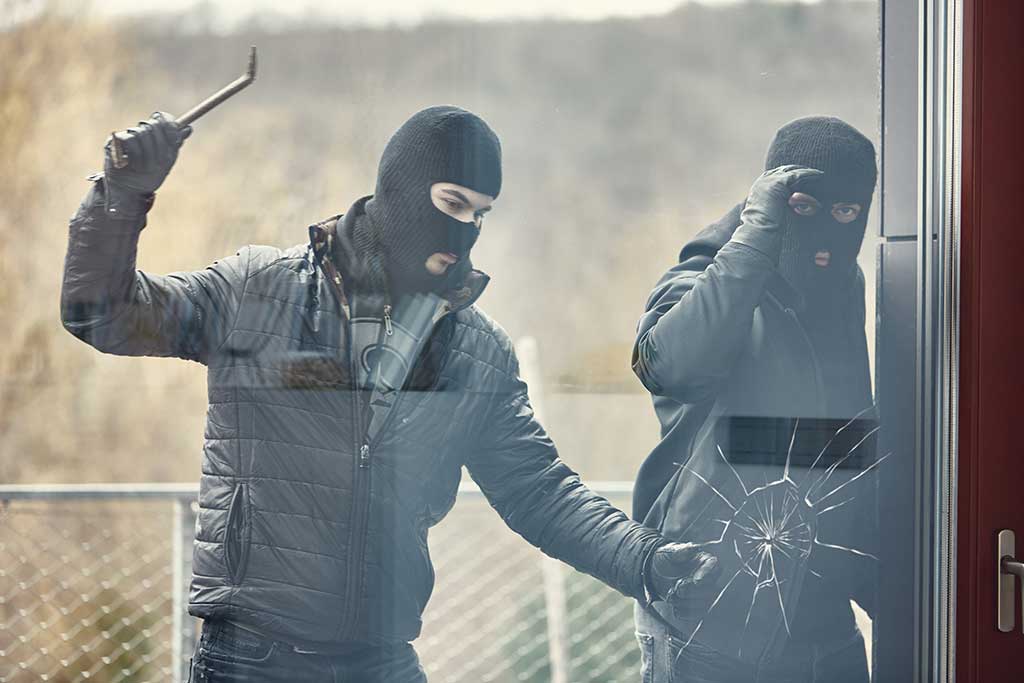 Two masked thieves breaking the glass to break in